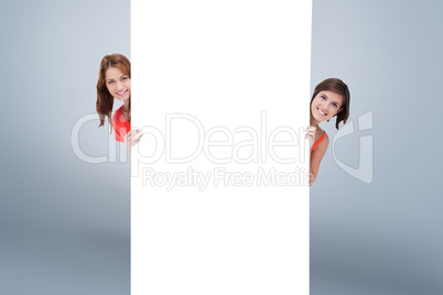 Composite image of teenage girls hiding behind a blank poster wh