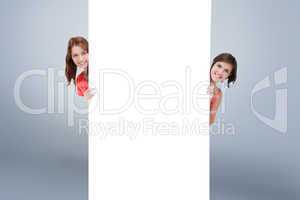 Composite image of teenage girls hiding behind a blank poster wh
