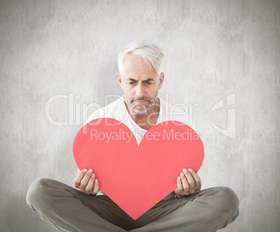 Composite image of upset man sitting holding heart shape