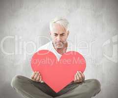 Composite image of upset man sitting holding heart shape