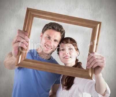 Composite image of couple holding frame ahead of them