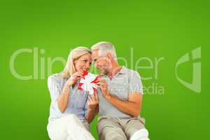 Composite image of happy couple sitting and holding present