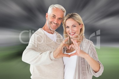 Composite image of happy couple forming heart shape with hands