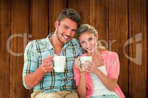 Composite image of attractive young couple sitting holding mugs