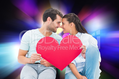 Composite image of cute couple sitting holding red heart