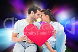 Composite image of cute couple sitting holding red heart