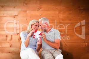 Composite image of happy couple sitting and holding present