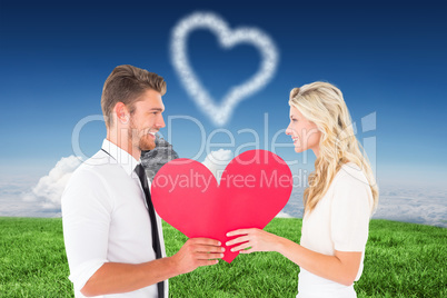 Composite image of attractive young couple holding red heart