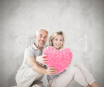 Composite image of happy couple sitting and holding heart pillow