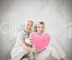 Composite image of happy couple sitting and holding heart pillow