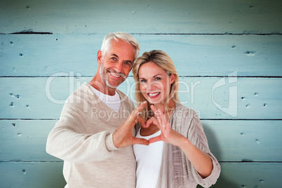 Composite image of happy couple forming heart shape with hands