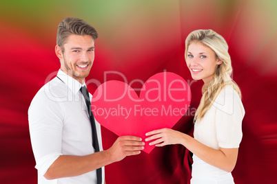 Composite image of attractive young couple holding red heart