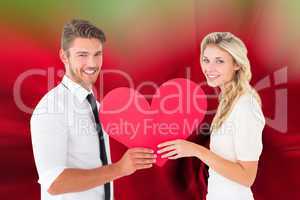 Composite image of attractive young couple holding red heart