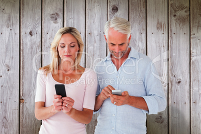 Composite image of happy couple texting on their smartphones