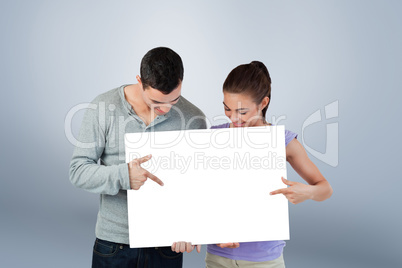 Composite image of young couple pointing at banner they are pres