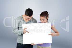 Composite image of young couple pointing at banner they are pres