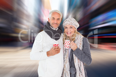 Composite image of happy couple in winter fashion holding mugs