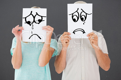 Composite image of couple holding paper over their faces