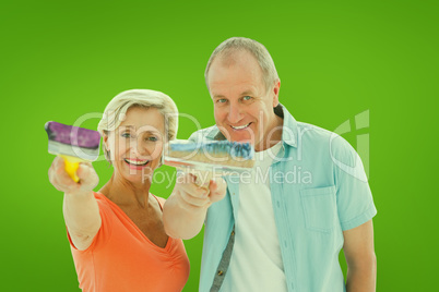 Composite image of happy older couple holding paintbrushes