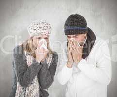 Composite image of sick couple in winter fashion sneezing