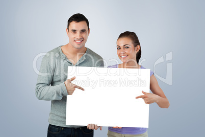 Composite image of smiling young couple pointing at sign they ar