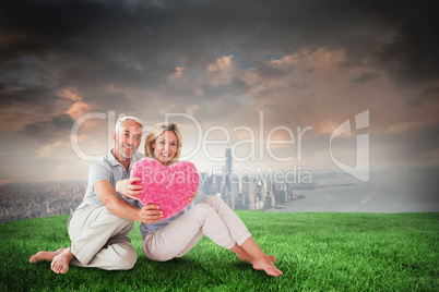 Composite image of happy couple sitting and holding heart pillow