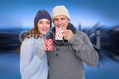 Composite image of happy couple in warm clothing holding mugs