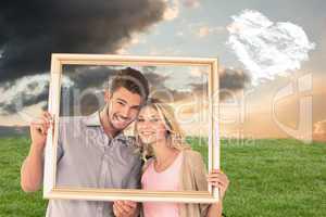 Composite image of attractive young couple holding picture frame