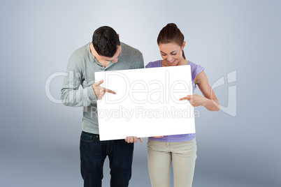 Composite image of young couple pointing at banner they are hold Composite image of young couple pointing at banner they are hold