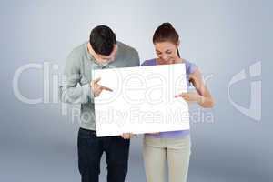 Composite image of young couple pointing at banner they are hold