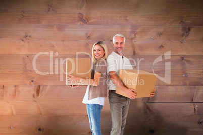 Composite image of happy couple holding moving boxes