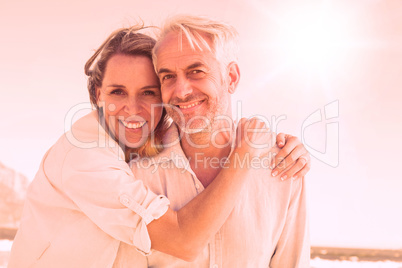 Attractive couple hugging at the beach smiling at camera