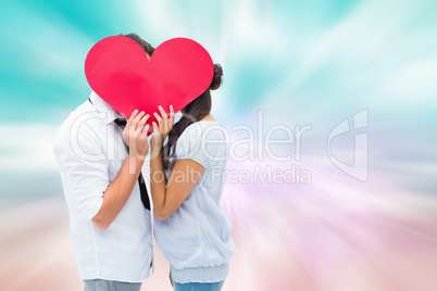 Composite image of couple covering their kiss with a heart