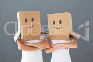 Composite image of couple wearing smiley face boxes on their hea