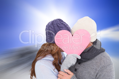 Composite image of couple in warm clothing holding heart