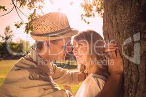 Cute smiling couple leaning against tree in the park