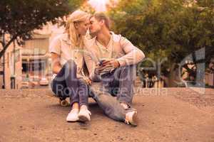 Hip young couple sitting on skateboard kissing