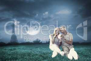 Composite image of happy couple sitting and holding present