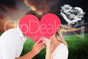 Composite image of attractive young couple kissing behind large