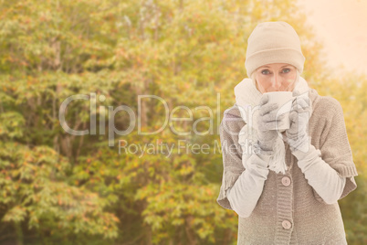 Composite image of woman in warm clothing holding mugs