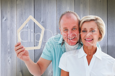 Composite image of happy older couple holding house shape