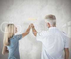 Composite image of happy couple painting wall with roller