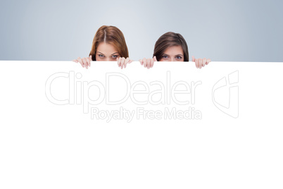 Composite image of two friends secretly hiding behind a blank po