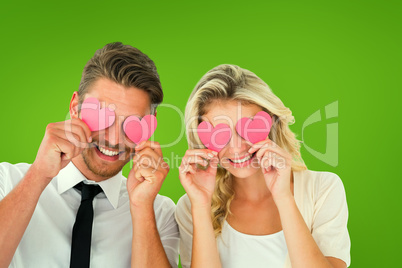 Composite image of attractive young couple holding pink hearts o