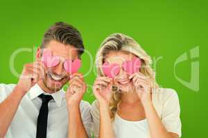 Composite image of attractive young couple holding pink hearts o