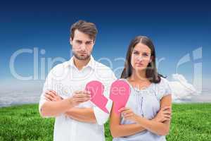 Composite image of upset couple holding two halves of broken hea