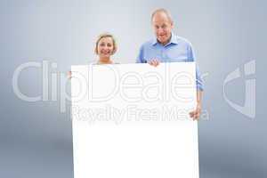 Composite image of mature couple smiling at camera holding card