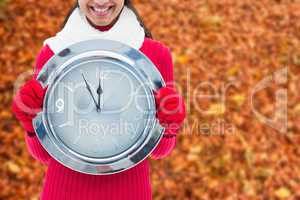 Composite image of festive brunette holding clock