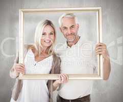 Composite image of happy couple holding a picture frame