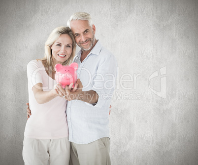 Composite image of happy couple showing their piggy bank